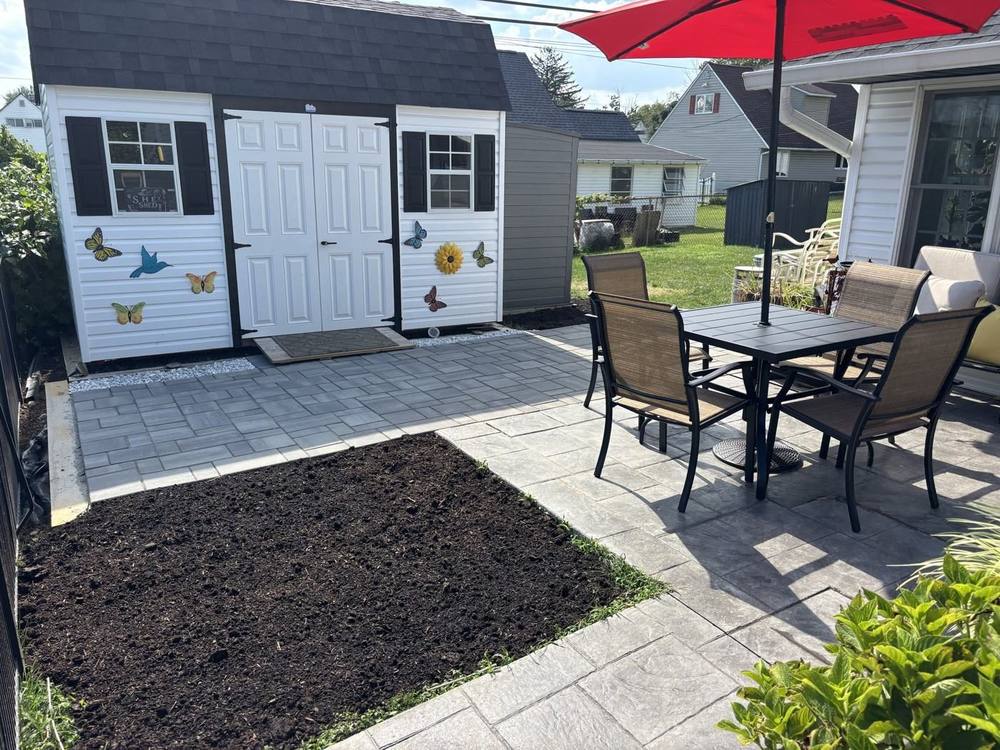 Gray paver pad in front of a shed joining a stamped concrete patio